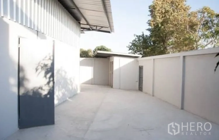 Warehouse for rent in Bang Phli, Samut Prakan - Walled outdoor yard beside the warehouse with a small service structure and doorway.