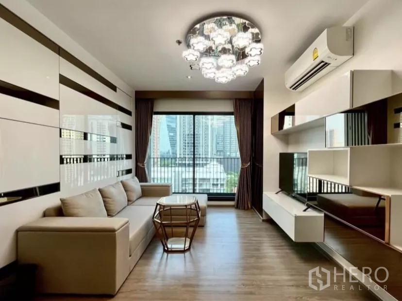 คอนโด ให้เช่าในWatthana, Bangkok - ห้องนั่งเล่นติดกระจกเต็มบาน มีระเบียงและวิวสกายไลน์ พร้อมโคมไฟและผนังทีวีเงาวาว