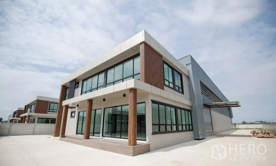 Factory for rent or sale in Bang Len, Nakhon Pathom - Modern two-storey factory with glass-fronted office and wide concrete driveway under blue sky.