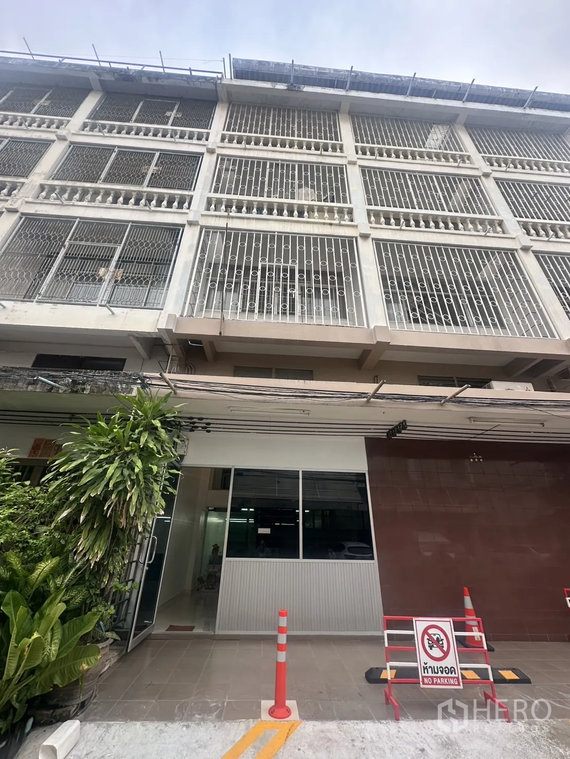 สำนักงาน ให้เช่าในKhlong Toei, Bangkok - อาคารสำนักงานหลายชั้นด้านหน้าเหล็กดัด ทางเข้าเป็นกระจก มีต้นไม้และป้ายห้ามจอด.