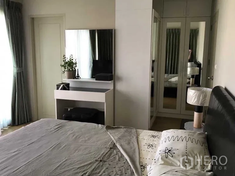 Condominium for rent in Watthana, Bangkok - Master bedroom with vanity, mirrored wardrobe, and soft natural light from a large window.