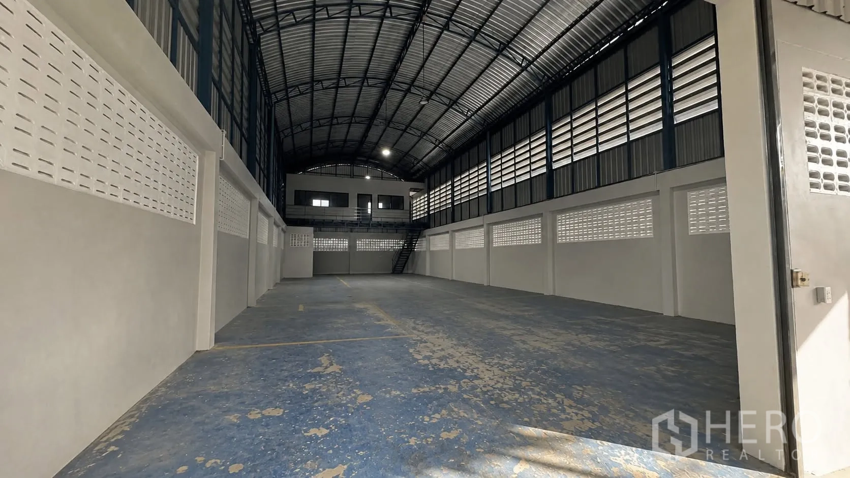 Warehouse for rent in Mueang Samut Prakan, Samut Prakan - Interior of the warehouse showing a high arched roof, ventilation blocks, and a mezzanine office with stairs.