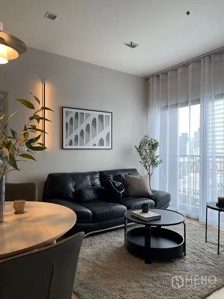 คอนโด ให้เช่าในWatthana, Bangkok - ห้องนั่งเล่นมีโซฟาหนังสีดำ โต๊ะกลางทรงกลม ต้นไม้ และระเบียงวิวเมือง