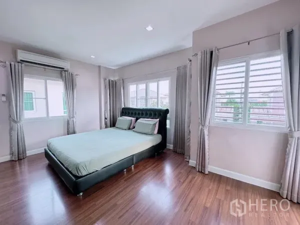 Detached House for rent in Prawet, Bangkok - Spacious master bedroom with large bed, wood floors, multiple windows, and air conditioning.
