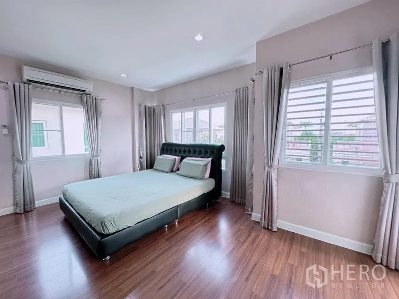 Detached House for rent in Prawet, Bangkok - Spacious master bedroom with large bed, wood floors, multiple windows, and air conditioning.