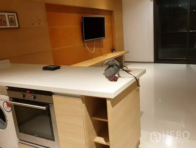 Condominium for sale in Khlong Toei, Bangkok - Open-plan living room with white island kitchen, built-in oven, and a sliding glass door to the balcony.