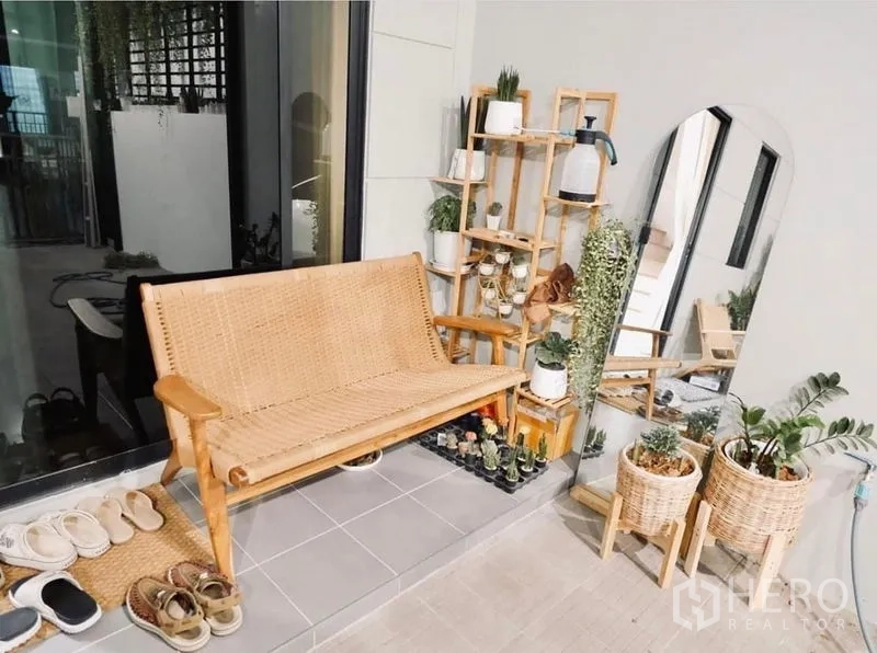Townhouse for rent in Bang Kapi, Bangkok - Cozy front patio with a rattan bench, potted plants, shelving, and a tall mirror.