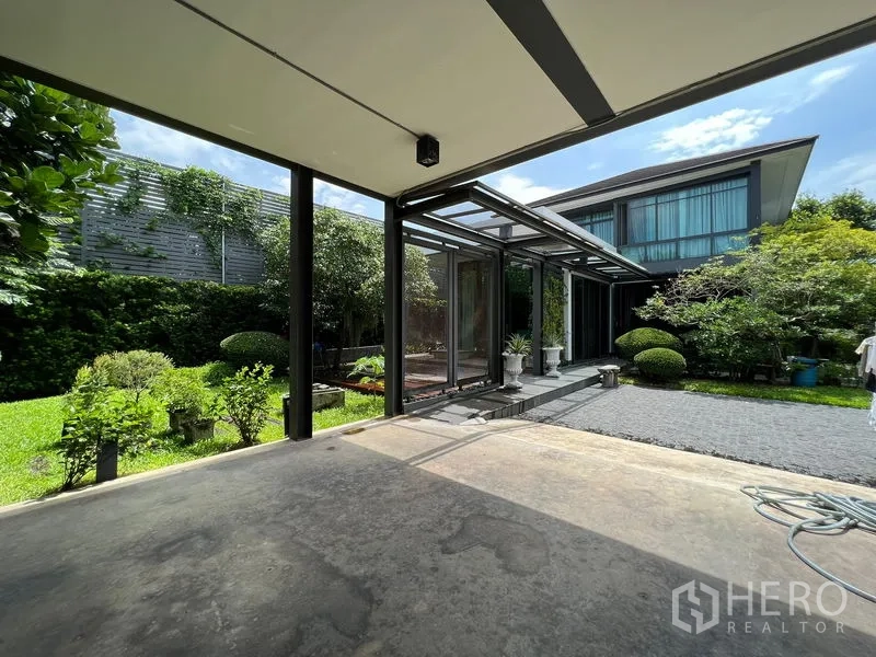 Detached House for sale in Bang Kapi, Bangkok - View from the carport toward the house with steel canopy and green hedges.