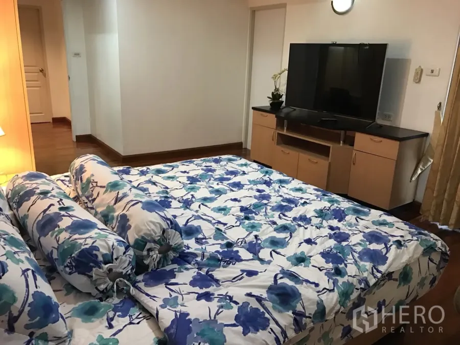 公寓 出租在Khlong Toei, Bangkok - 主卧配花纹床品、电视柜与温暖木地板。