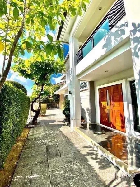 Detached House for sale in Saphan Sung, Bangkok - Modern house side walkway with shade trees, trimmed hedge and wide double wooden entrance.