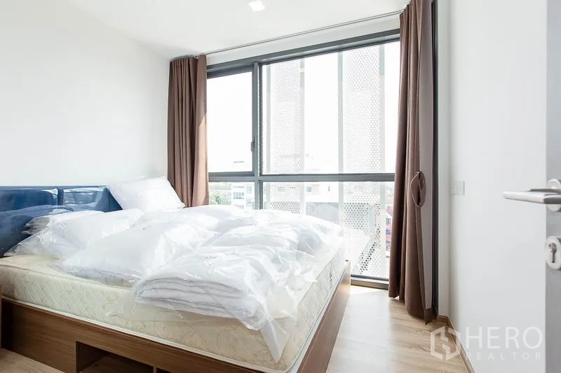 Condominium for rent in Watthana, Bangkok - Sunlit bedroom with large windows, blackout curtains and a queen bed base.