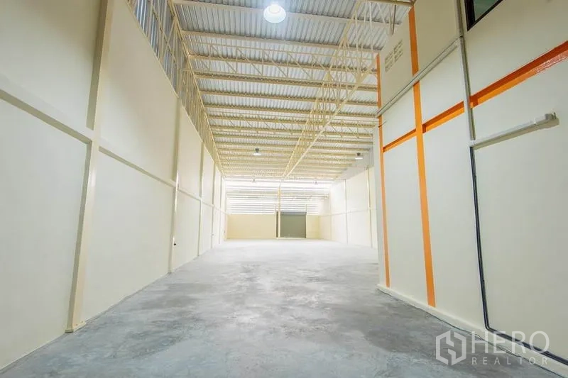 Factory for sale in Bang Sao Thong, Samut Prakan - Bright storage hall with tall clearance, insulated metal roof, ventilation panels and a shutter door at the far end.