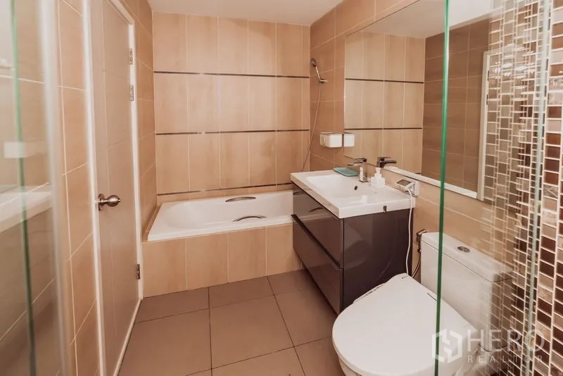 Condominium for rent in Sathon, Bangkok - Second bathroom featuring a built-in bathtub, large mirror, and storage vanity.