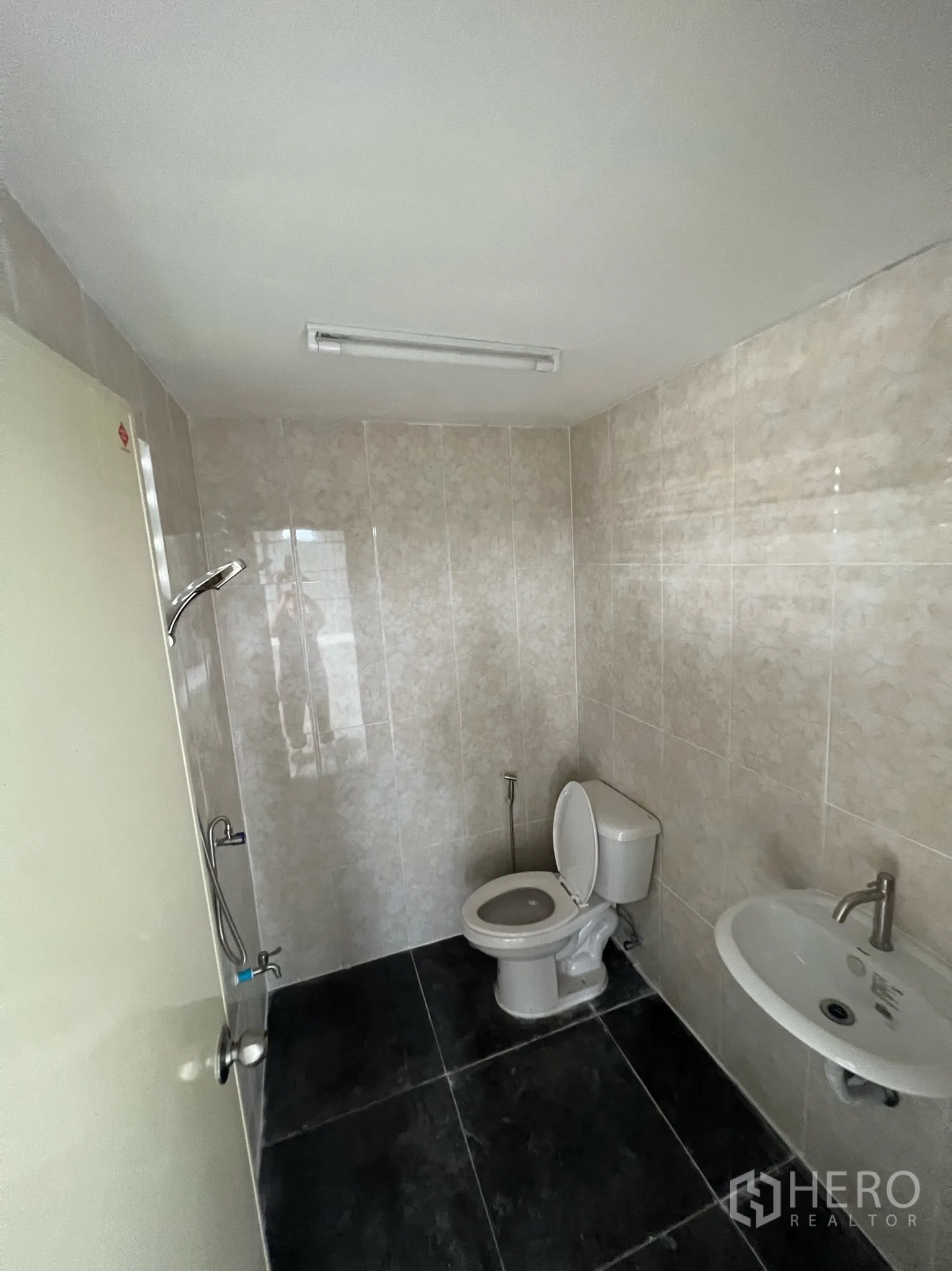 货栈 出租在Lam Luk Ka, Pathum Thani - 仓库内铺砖卫生间，配坐便器、洗手盆和喷枪。