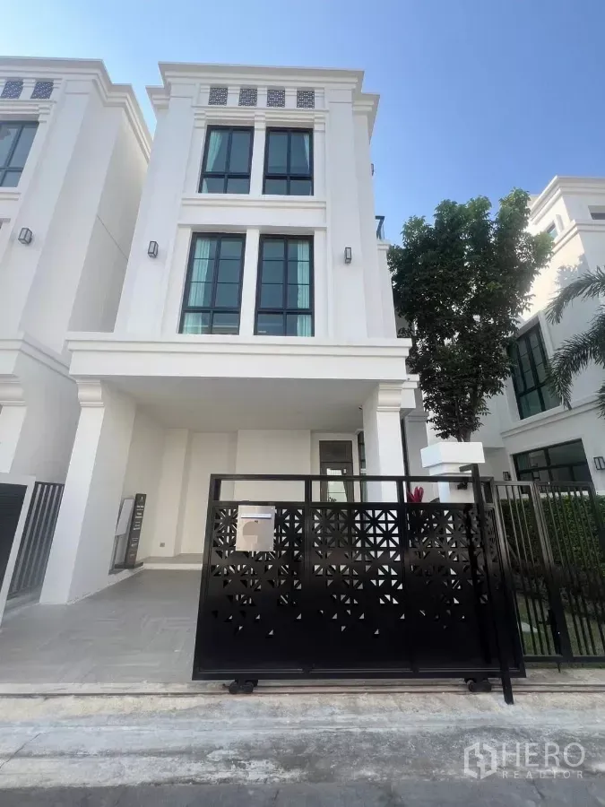 Detached House for rent in Lat Phrao, Bangkok - Three-storey detached house with modern white facade, tall black-framed windows and a black sliding gate.