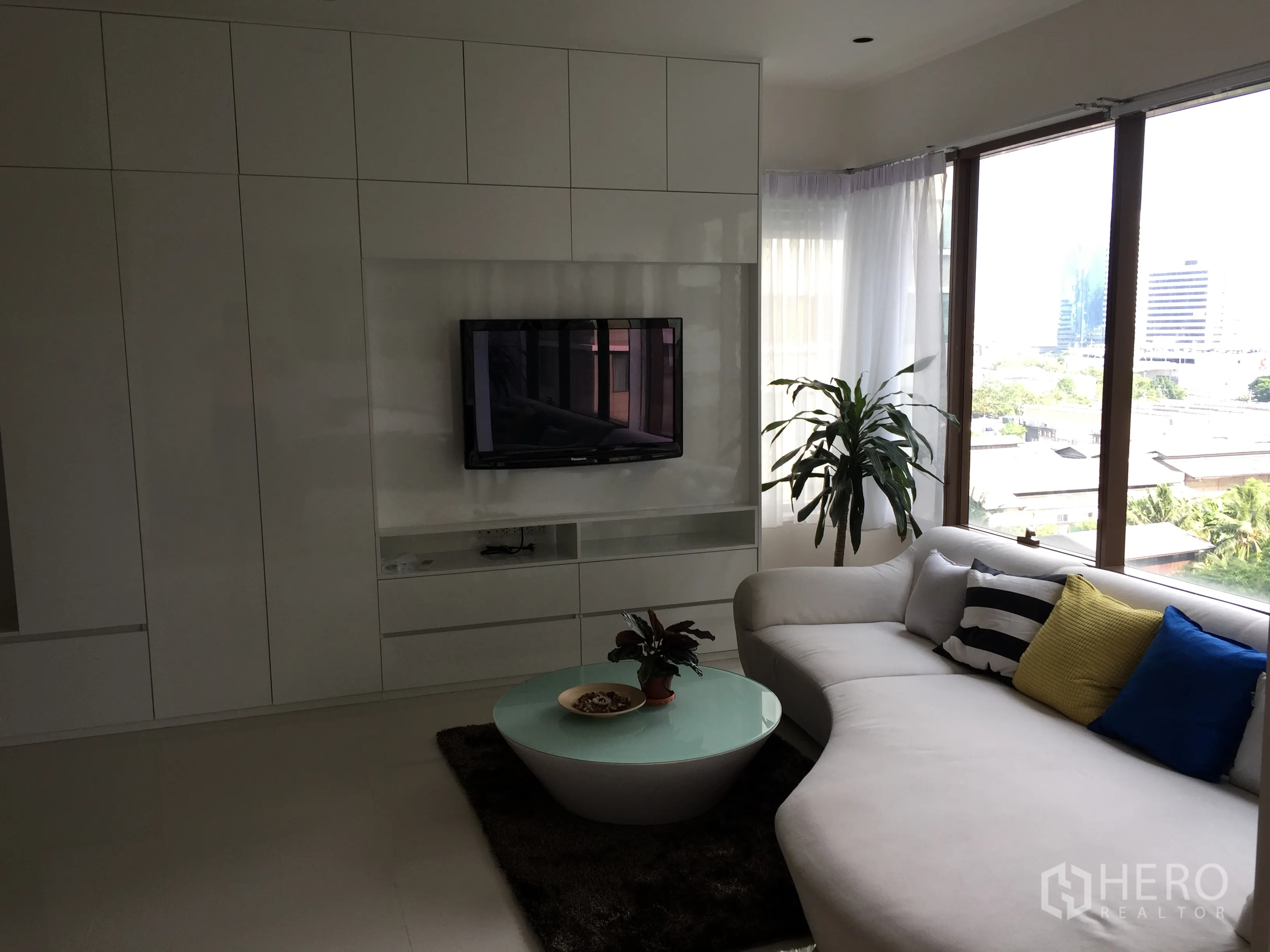 คอนโด ให้เช่าในKhlong Toei, Bangkok - ห้องนั่งเล่นมีผนังบิวท์อินทีวี โซฟาตัวแอล ไม้ประดับ และหน้าต่างพาโนรามาวิวเมือง