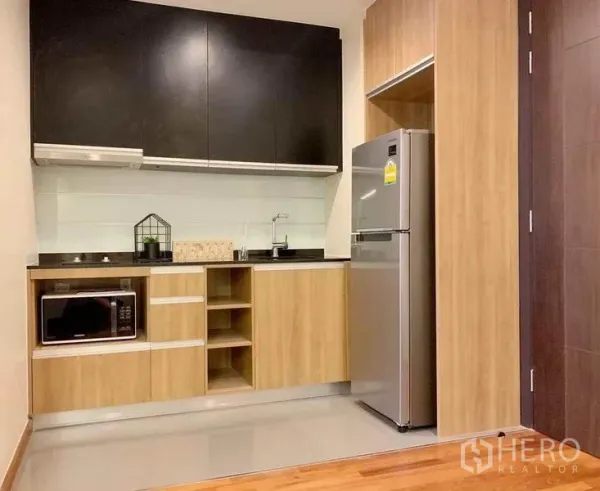 Condominium for sale in Ratchathewi, Bangkok - Compact kitchen with wood cabinetry, cooktop, microwave and full-size fridge.