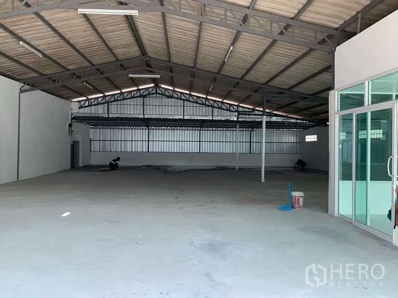 货栈 出租在Mueang Pathum Thani, Pathum Thani - 仓库内部空间开阔，高钢梁屋顶，混凝土地面，玻璃入口门。