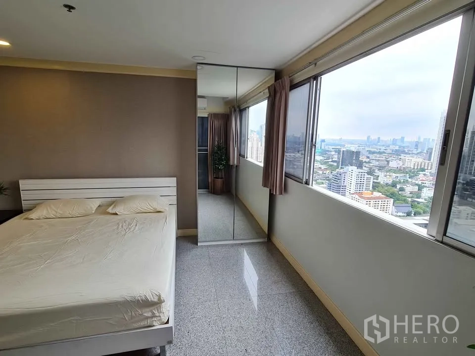 Condominium for rent in Khlong Toei, Bangkok - Bedroom with large windows, mirror-front wardrobe and city skyline view.