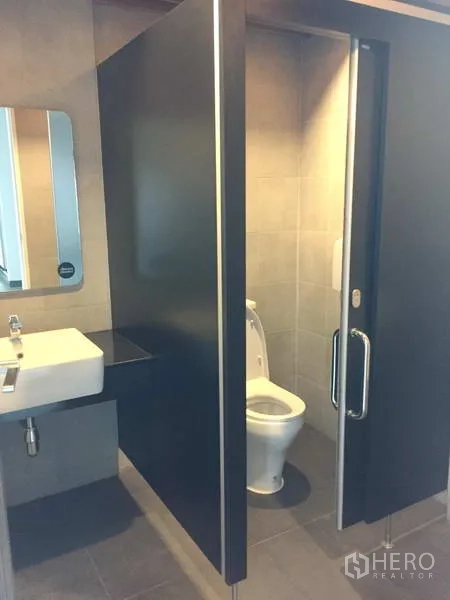 Office Space for rent in Khlong Toei, Bangkok - Modern restroom with a toilet cubicle, sliding partition door, sink, and wall mirror.