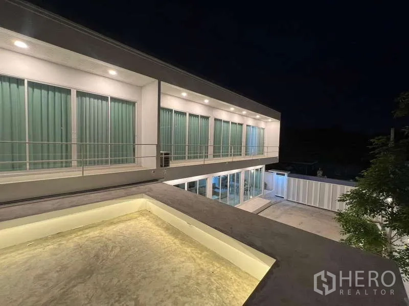 บ้าน ให้เช่าในLat Krabang, Bangkok - อาคารสองชั้นทรงโมเดิร์นยามค่ำ พร้อมระเบียงและผนังกระจกสว่างไสว