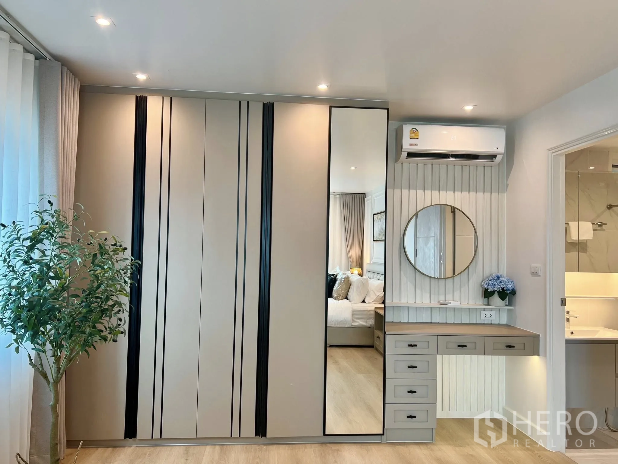 Condominium for rent or sale in Yan Nawa, Bangkok - Built-in wardrobe with mirrored door and a vanity desk under a wall-mounted air conditioner in a modern condo bedroom.