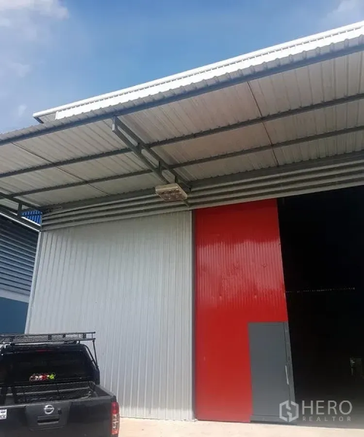 货栈 出租在Prawet, Bangkok - 仓库外立面，红灰双色金属推拉门，带雨棚及装卸/停车区。