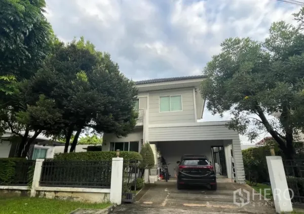 บ้าน ขายในMin Buri, Bangkok - บ้านเดี่ยวสองชั้นพร้อมรั้ว หน้าโครงการมีโรงจอดรถและทางเข้ารถ รายล้อมด้วยต้นไม้ เขตมีนบุรี กรุงเทพฯ