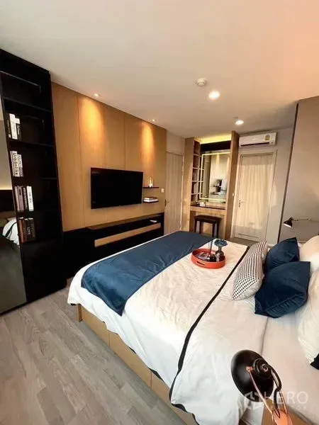 Condominium for sale in Bang Sue, Bangkok - Bedroom with wall-mounted TV, built-in wardrobe and vanity, warm wood flooring and downlights.