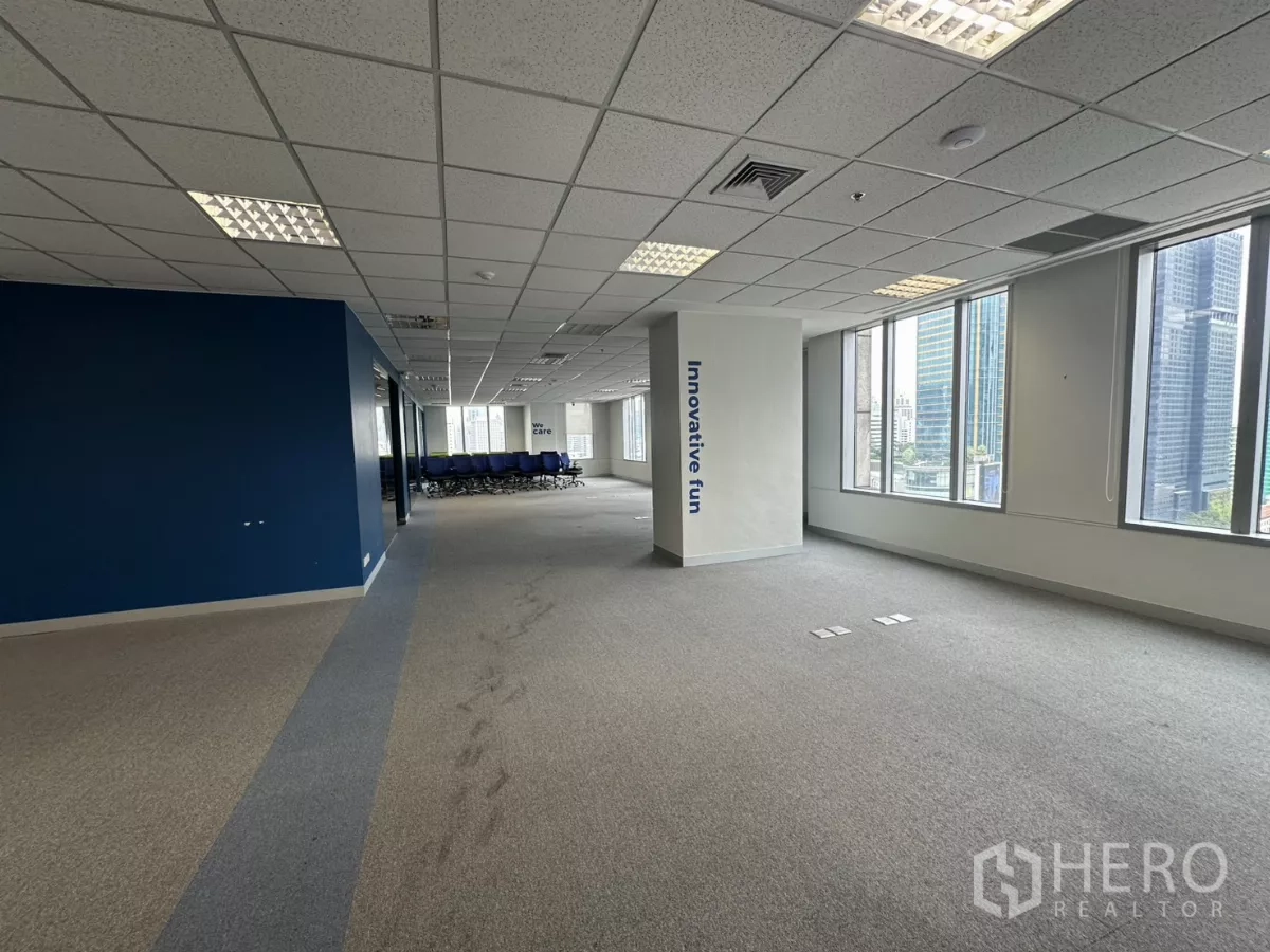 办公空间 出租在Watthana, Bangkok - 临窗开放走道与蓝色特征墙，窗外城市楼宇。