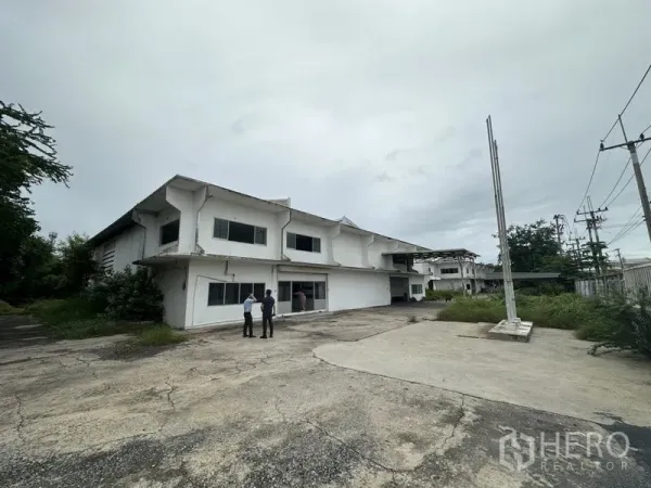 Factory for rent or sale in Khlong Luang, Pathum Thani - Front yard and parking apron of the two-storey factory building with wide driveway.