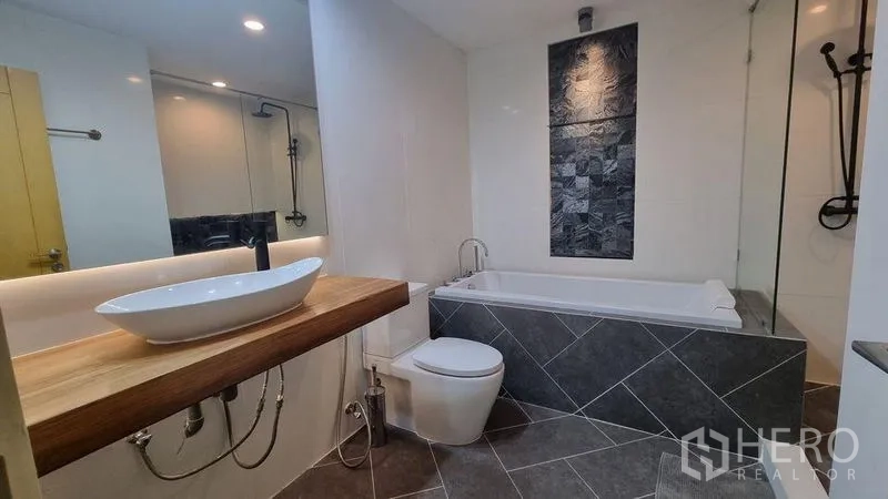 คอนโด ให้เช่าในWatthana, Bangkok - ห้องน้ำที่มีอ่างอาบน้ำ อ่างล้างหน้าแบบวางบนเคาน์เตอร์ไม้ และกระเบื้องสีเทา