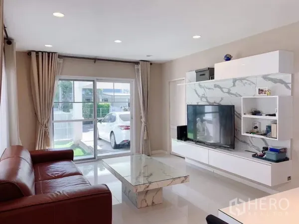 独立式住宅 出租或出售在Bang Phli, Samut Prakan - 客厅面向推拉玻璃门，可见车棚与小草坪