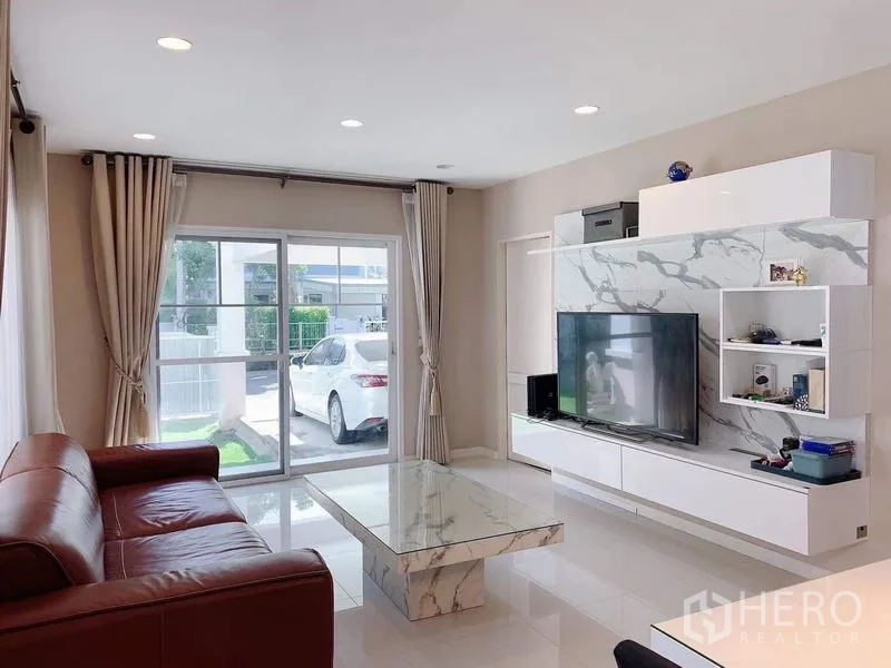 独立式住宅 出租或出售在Bang Phli, Samut Prakan - 客厅面向推拉玻璃门，可见车棚与小草坪