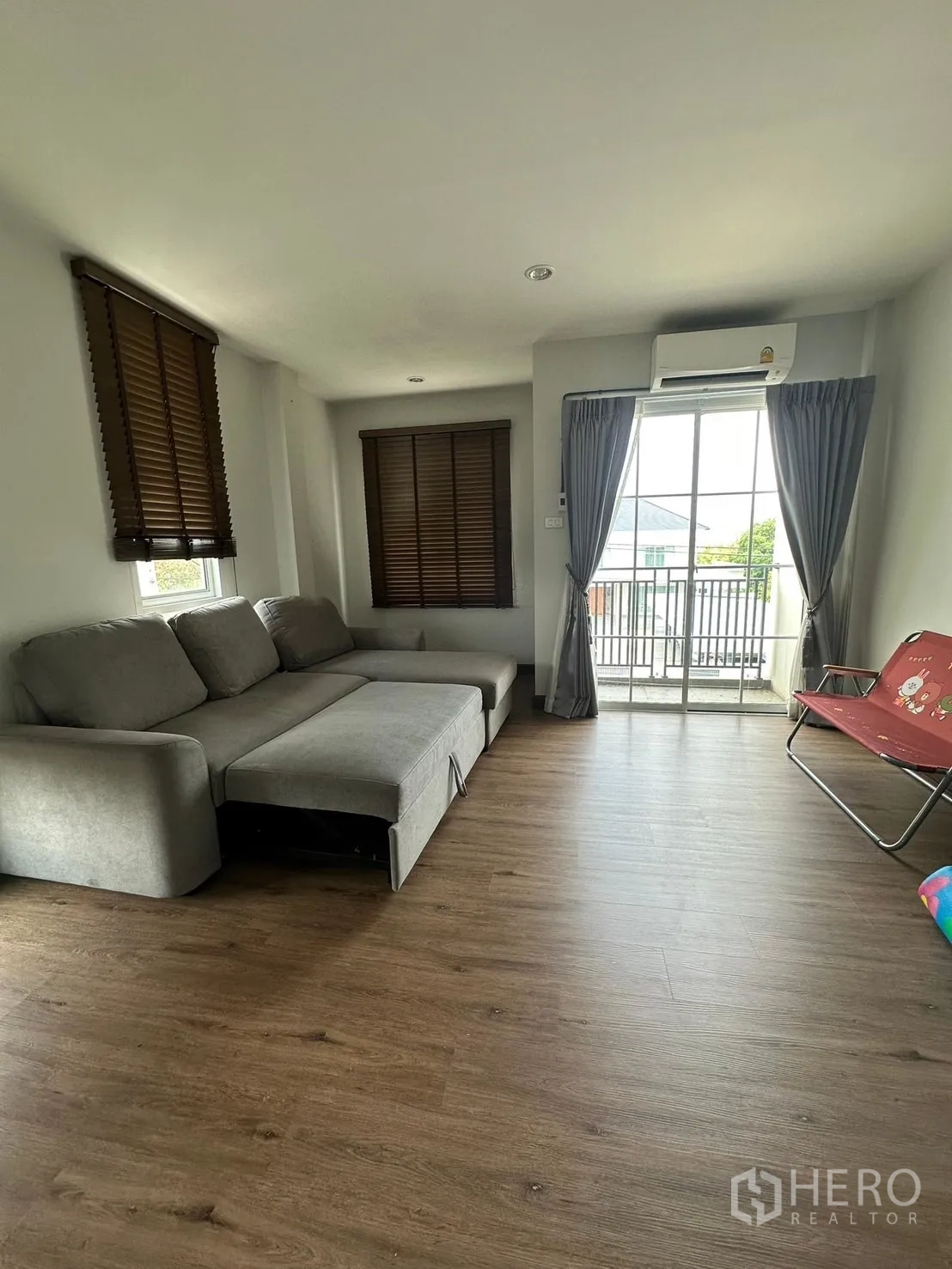 Home Office for rent in Khlong Luang, Pathum Thani - Living or lounge room with grey sectional sofa, wood-look floor and balcony.
