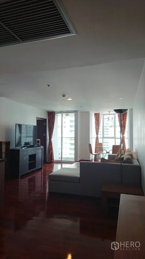 Condominium for rent in Pathum Wan, Bangkok - Bright living room with L-shaped sofa, TV console and floor-to-ceiling windows opening to a balcony with city views.