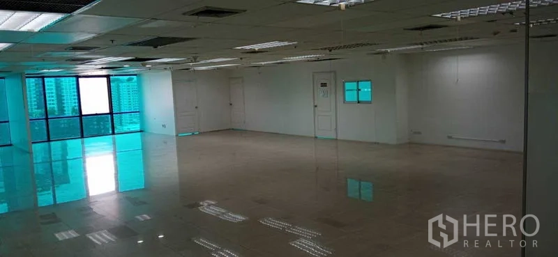 办公空间 出租在Huai Khwang, Bangkok - 空置办公室，大幅镀膜窗、多个房门与反光地面，悬挂天花板。
