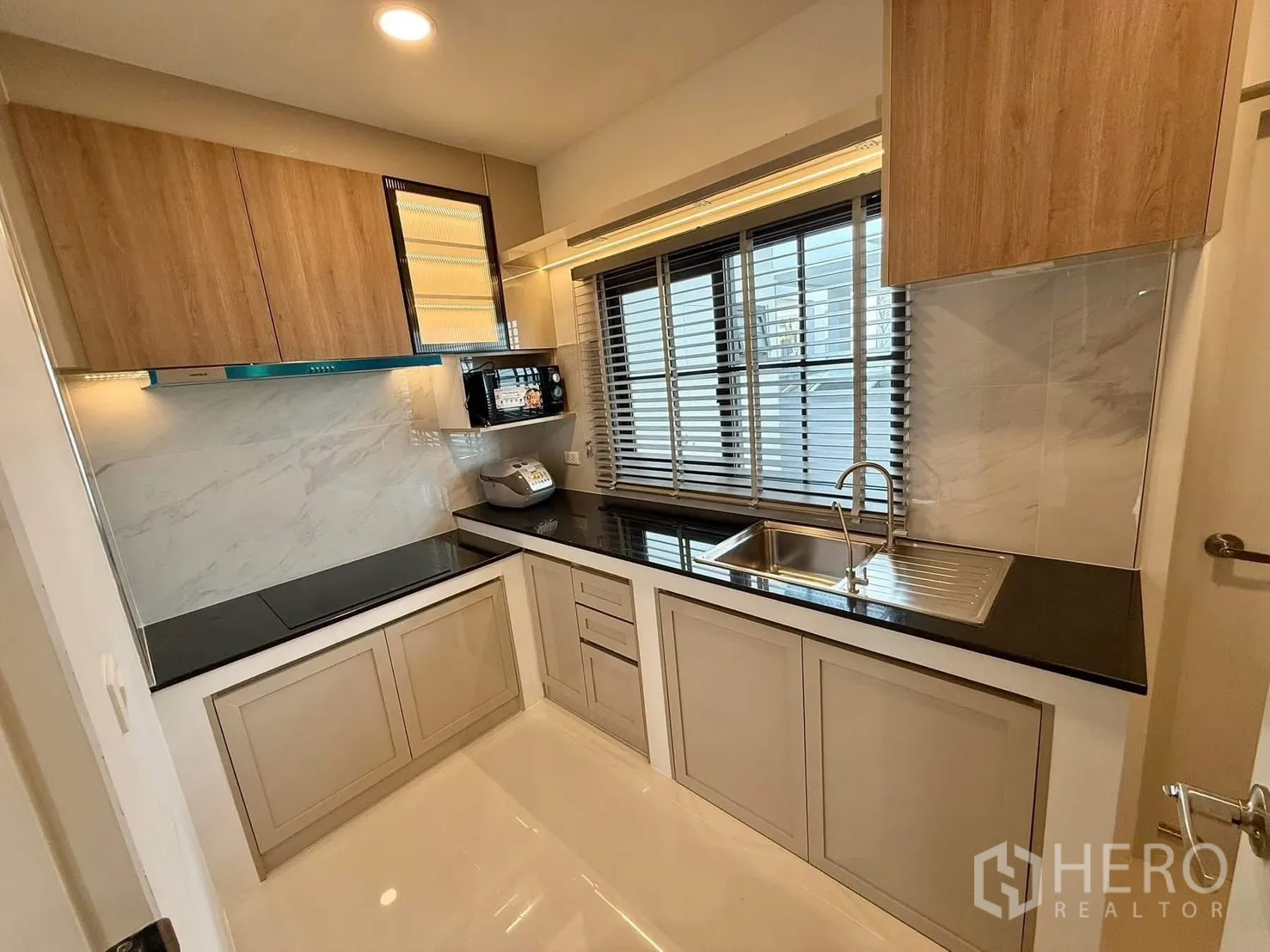 Detached House for rent in Bang Phli, Samut Prakan - Compact U-shaped kitchen with black countertops, wood cabinets, blinds, sink and cooktop.