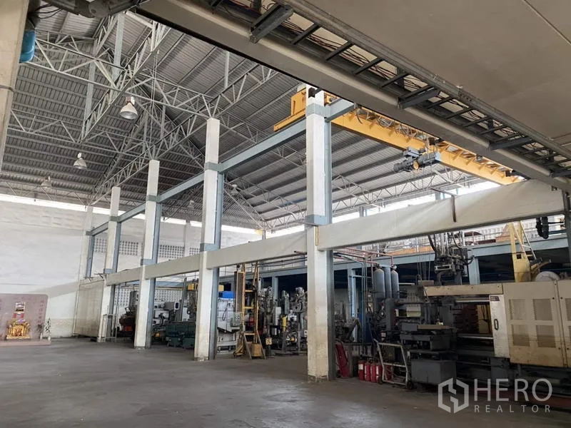 Factory for sale in Khlong Luang, Pathum Thani - Manufacturing zone featuring an overhead crane and machinery beneath a tall roof.