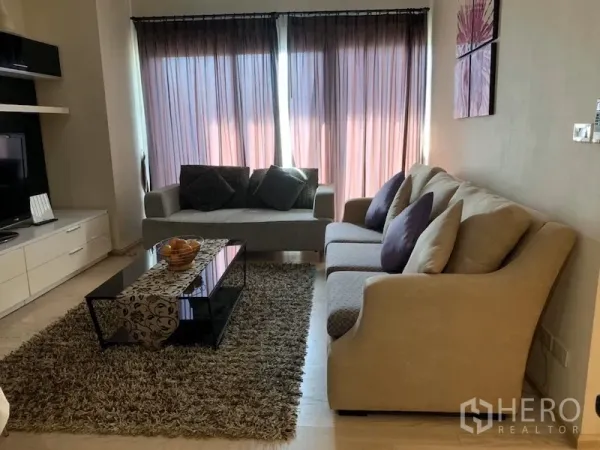 คอนโด ให้เช่าในKhlong Toei, Bangkok - ห้องนั่งเล่นอบอุ่น โซฟาสองตัว พรมขนฟู โต๊ะกลางกระจก และชั้นวางทีวีข้างหน้าต่างติดม่าน