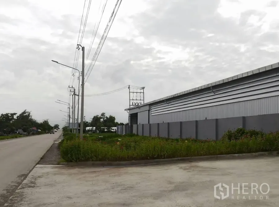 货栈 出租在Lam Luk Ka, Pathum Thani - 临路仓库外观，灰色金属墙体与围墙，电线杆成排，宽阔混凝土出入口