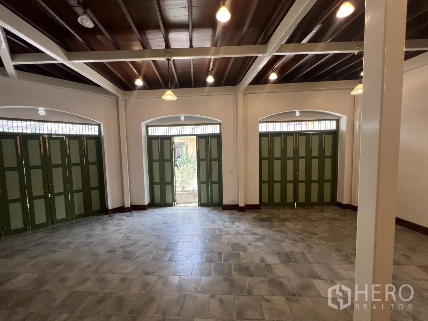 Shophouse for rent in Samphanthawong, Bangkok - Ground-floor sales hall with high ceilings, exposed beams, pendant lights and three wide green folding shopfront doors.