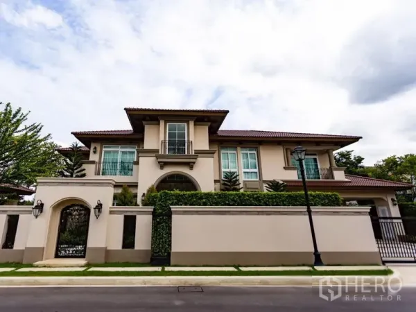 独立式住宅 出租在Mueang Samut Prakan, Samut Prakan - 两层独栋别墅外观，高墙与铁艺大门，修剪整齐的绿篱。