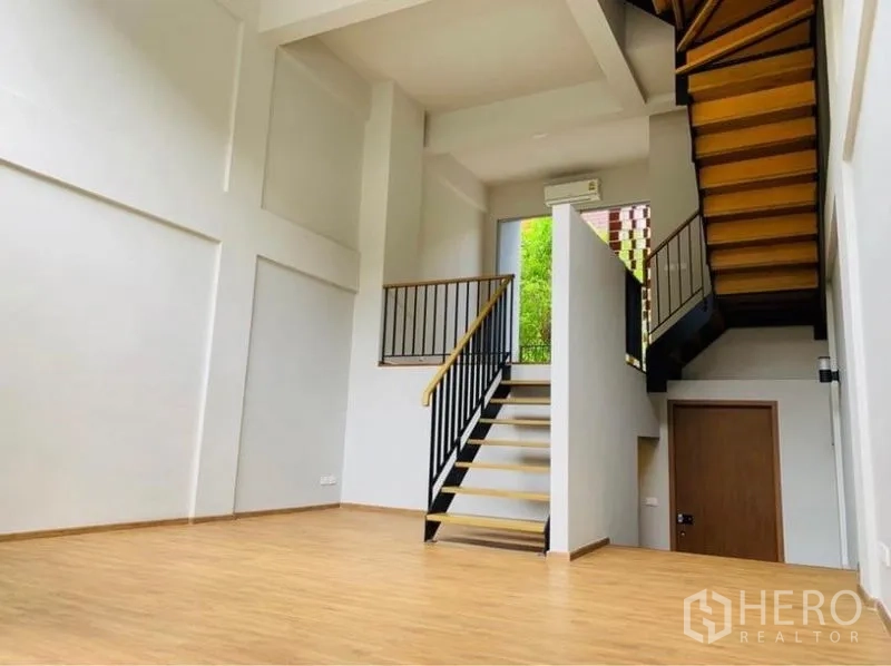 Home Office for rent - Double-height living area with wood floors, open staircase and large window bringing in greenery.