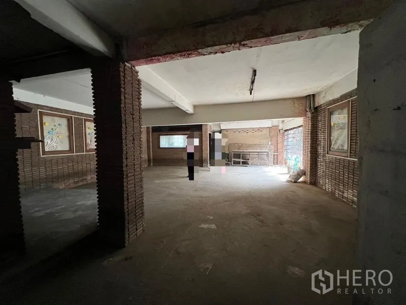 Shophouse for rent or sale in Bang Khen, Bangkok - Large open-plan ground floor with brick pillars, concrete floor and roller gate.