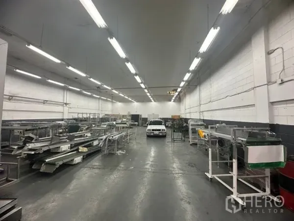 Factory for rent or sale in Khlong Luang, Pathum Thani - Spacious production hall with high ceiling, bright strip lighting and concrete floor.