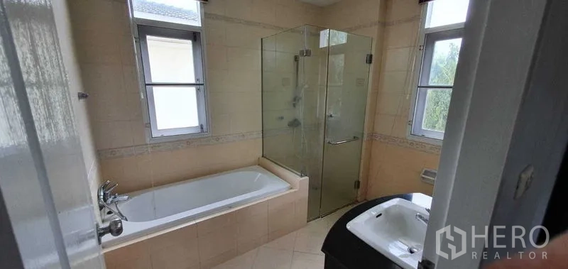 Detached House for rent in Prawet, Bangkok - Bathroom with bathtub, glass-enclosed shower and twin windows for ventilation.