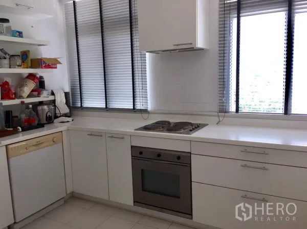 Condominium for rent in Watthana, Bangkok - Bright white L-shaped kitchen with oven, electric hob, dishwasher and large windows with blinds.