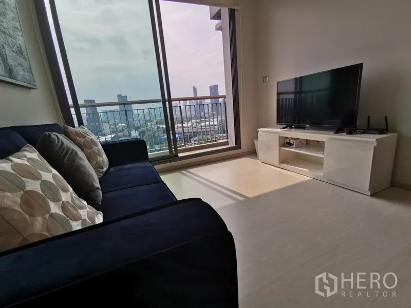 Condominium for rent in Khlong Toei, Bangkok - Cozy TV corner and sofa beside a balcony that captures wide city views.