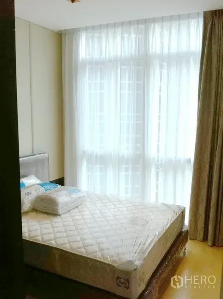 Condominium for rent in Pathum Wan, Bangkok - Bright second bedroom with large window, sheer drapes, and natural light on light wood floors.